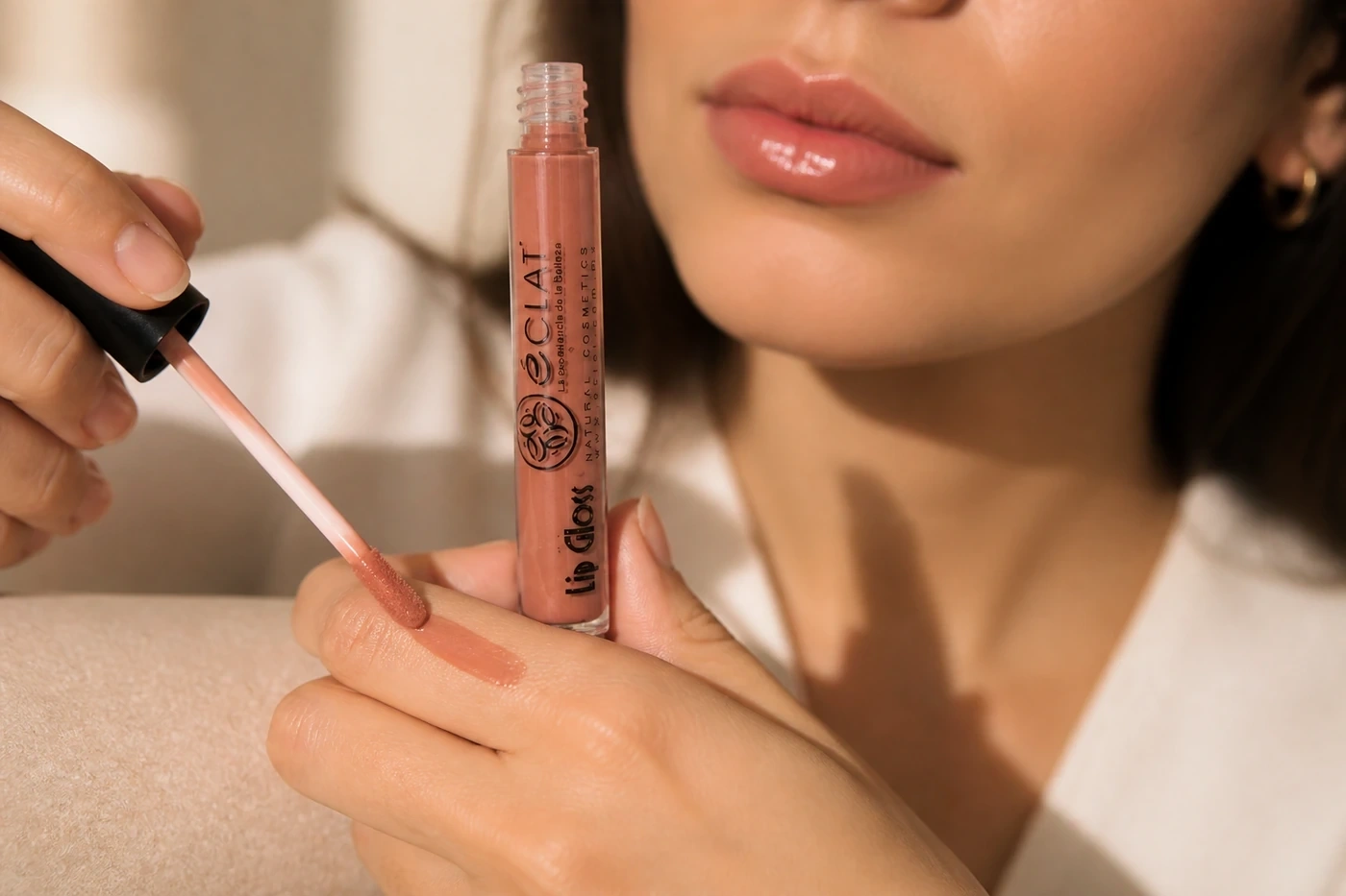 Lip gloss Éclat nude con aplicador y muestra de brillo sobre la mano